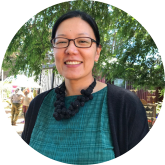 Portrait of Joanna Eun, a person with black hair pulled back wearing glasses, a green top, black cardigan, and a black necklace.